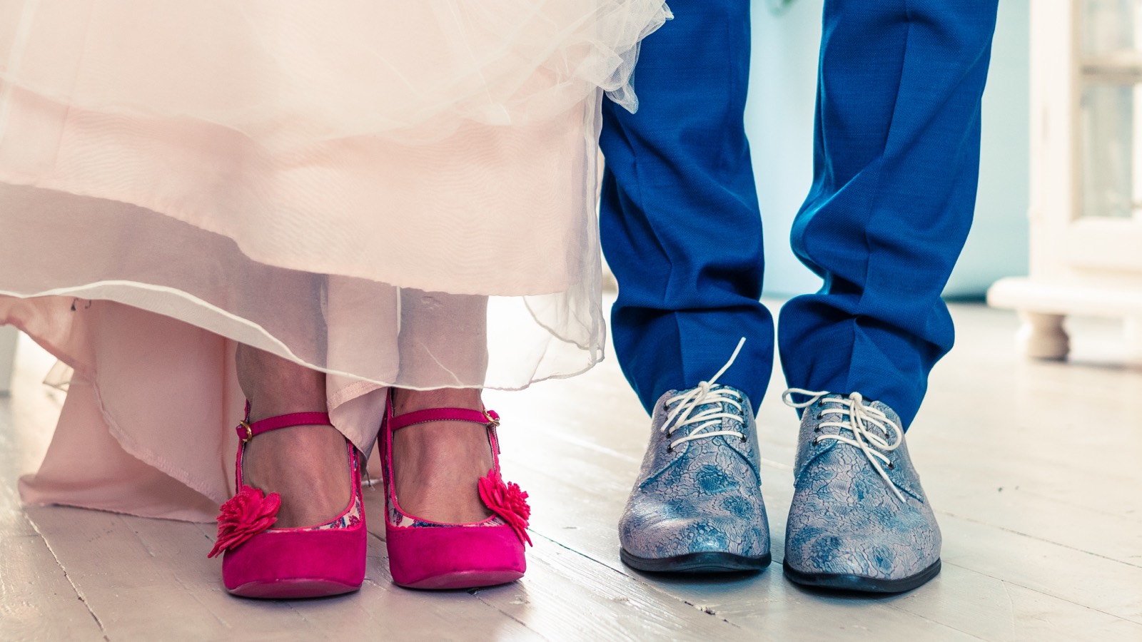 Roze schoenen van de bruid naast de blauwe bloemenschoenen van de bruidegom