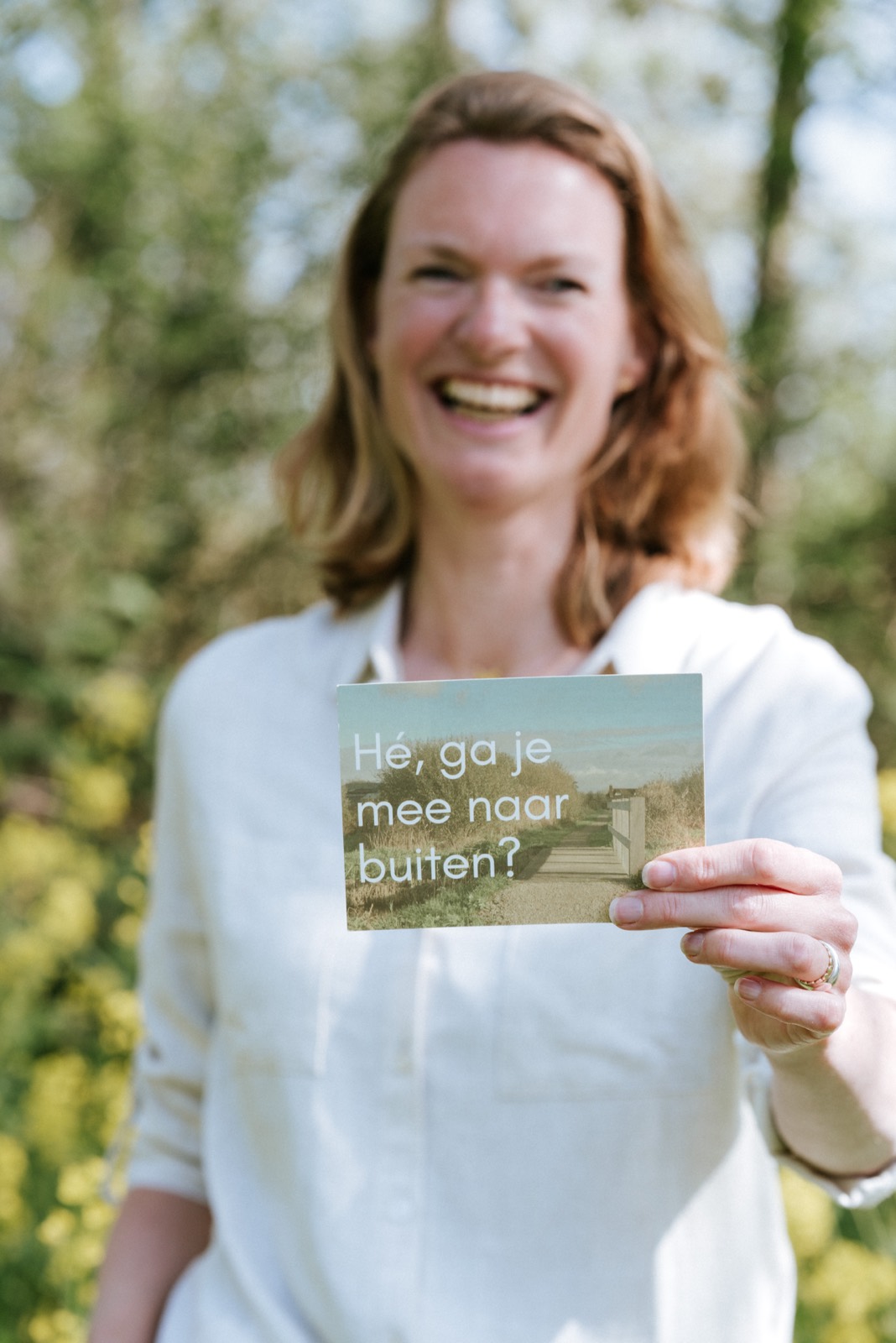 Wandelcoach Ellen houdt lachend een kaart vast met de tekst: ga je mee naar buiten?