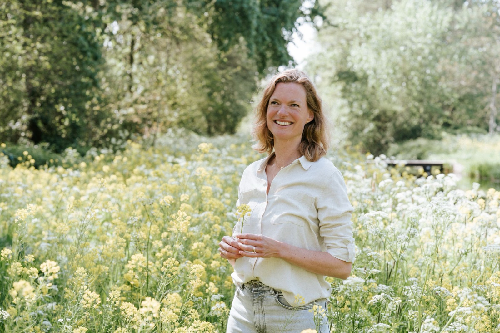 Wandelcoach Ellen lacht tussen gele en witte veldbloemen