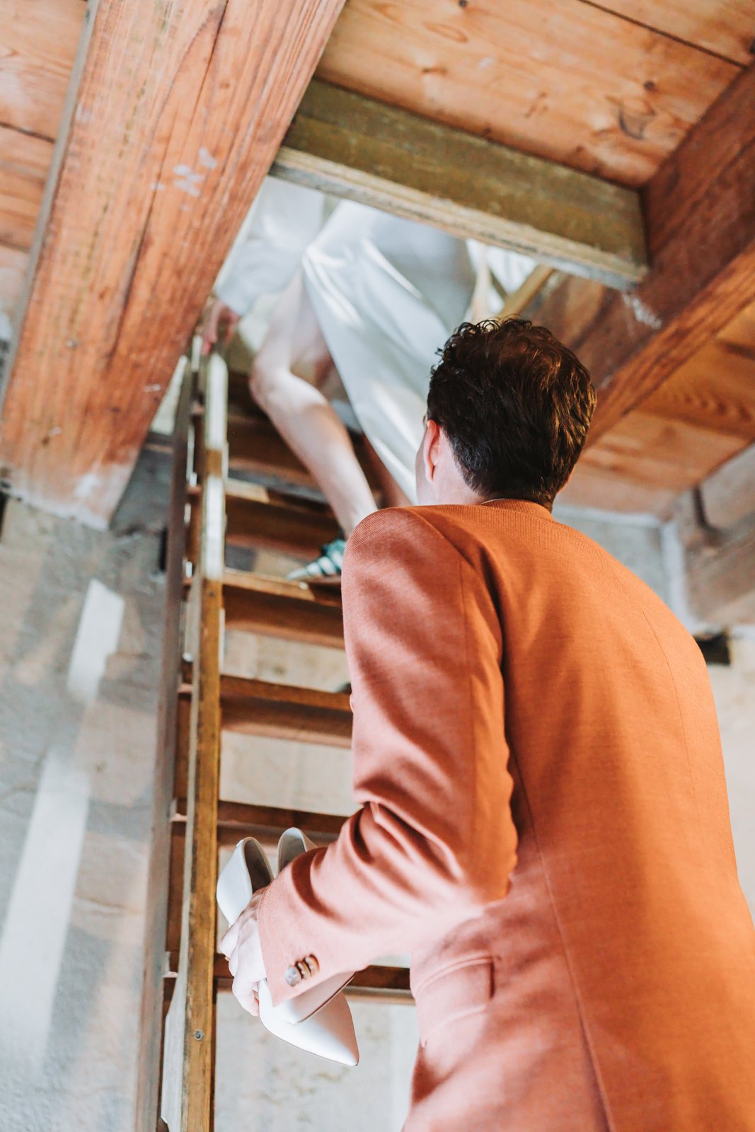 Bruid klimt een houten ladder op, de bruidegom volgt