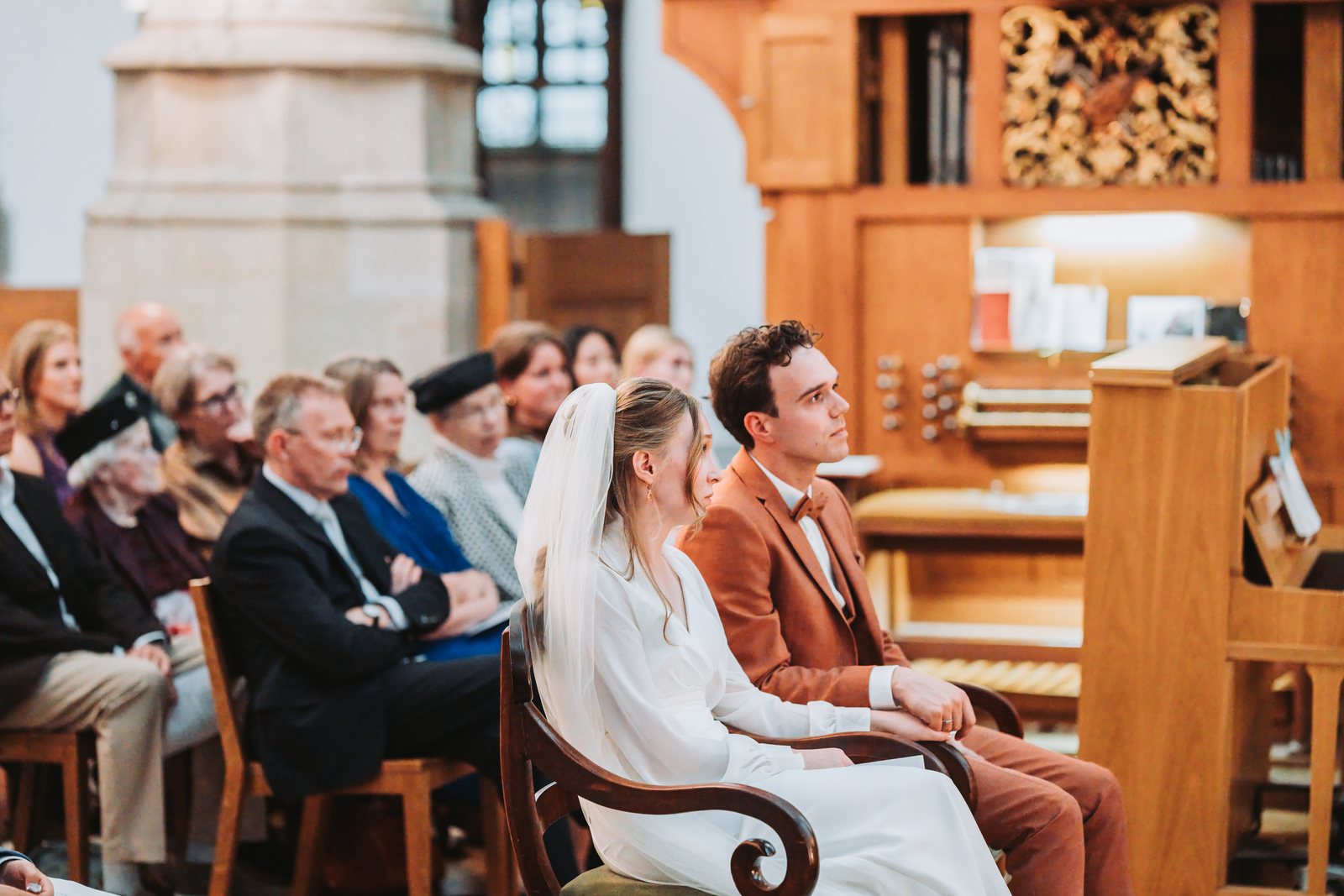 Bruidspaar luistert tijdens de ceremonie, met het orgel op de achtergrond