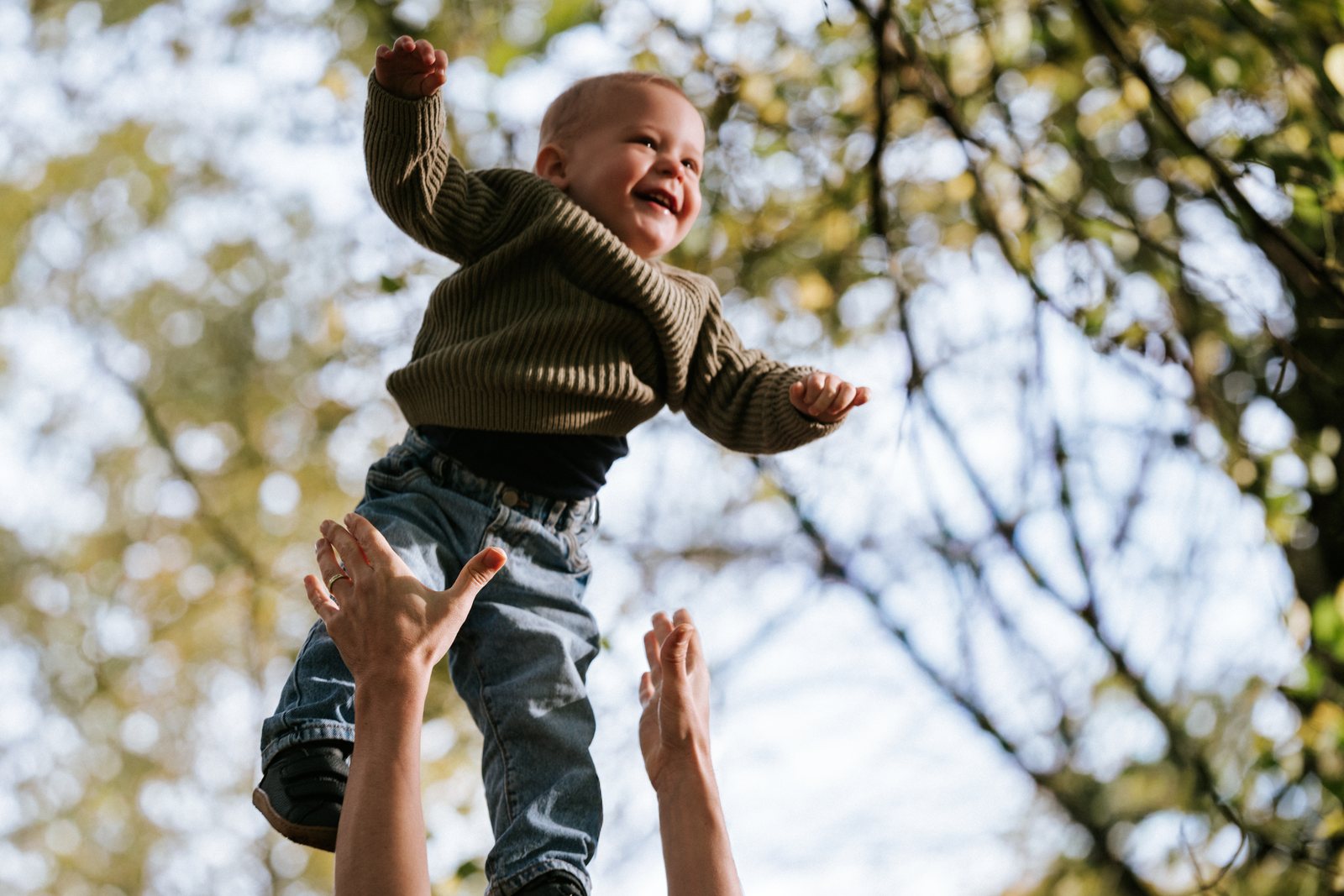 Zoontje vliegt lachend de lucht in onder de herfstbomen