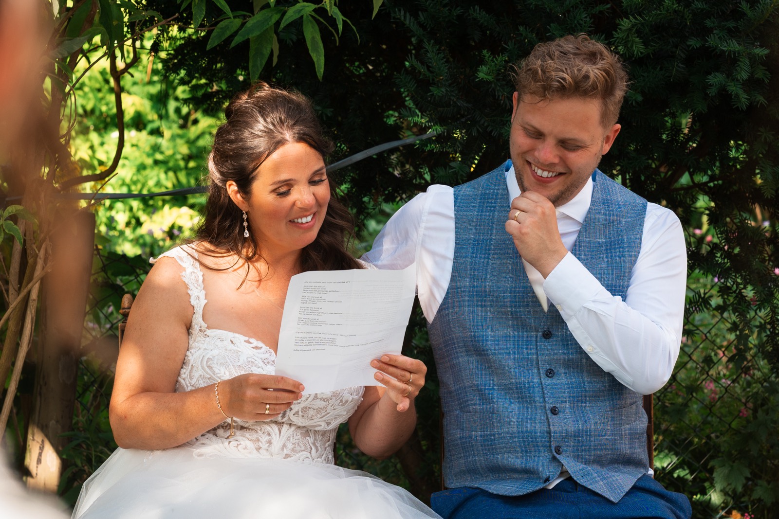 Bruidspaar leest lachend een liedtekst voor in de tuin