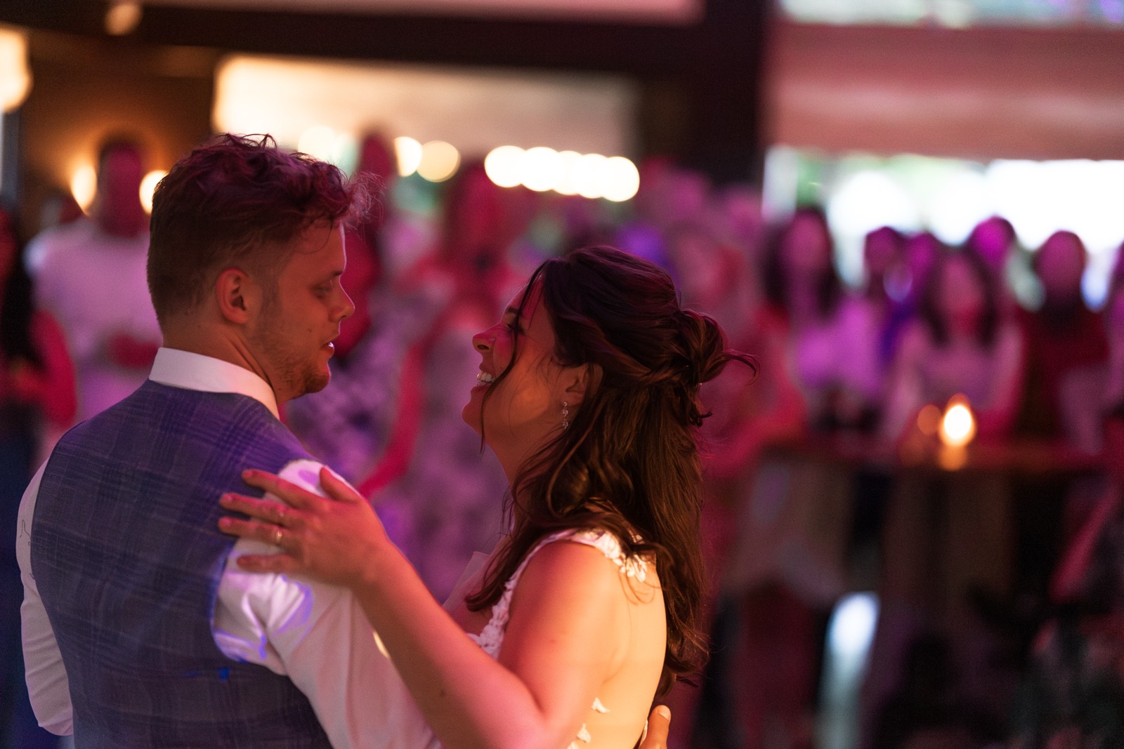 Bruidspaar danst dicht tegen elkaar in roze licht