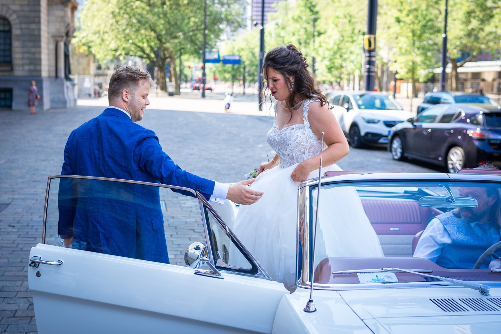 Bruidegom helpt de bruid in de witte Mustang
