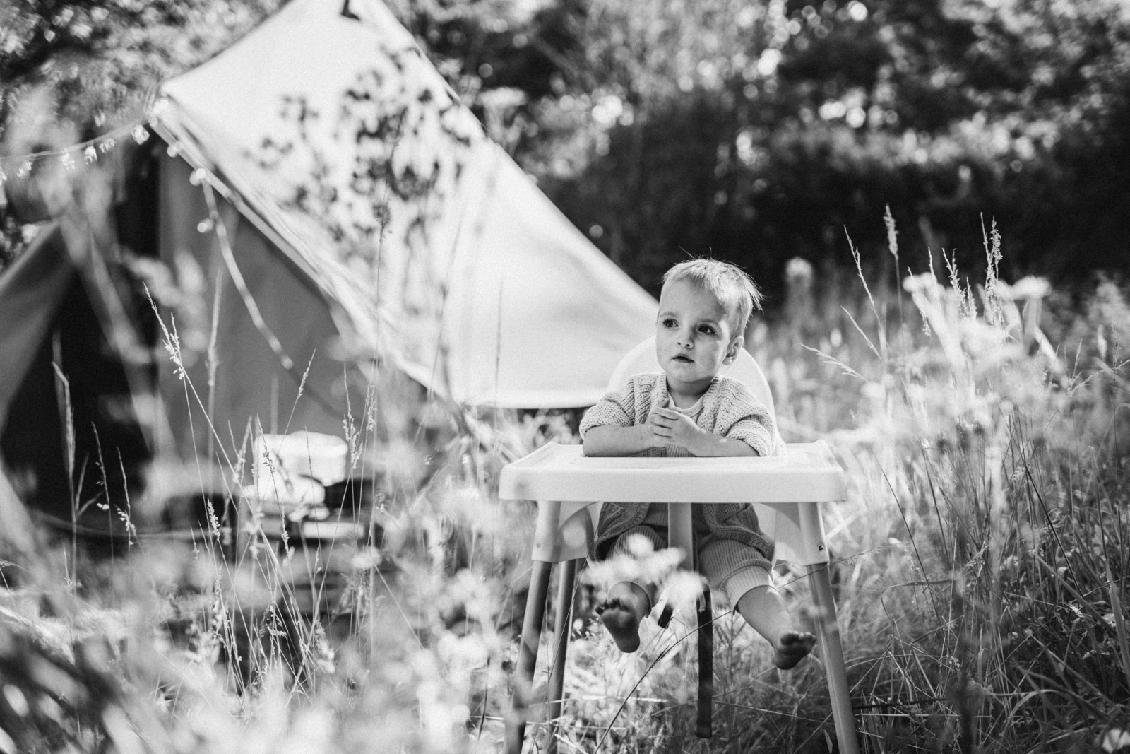 Meisje in een kinderstoel tussen hoog gras bij een tent