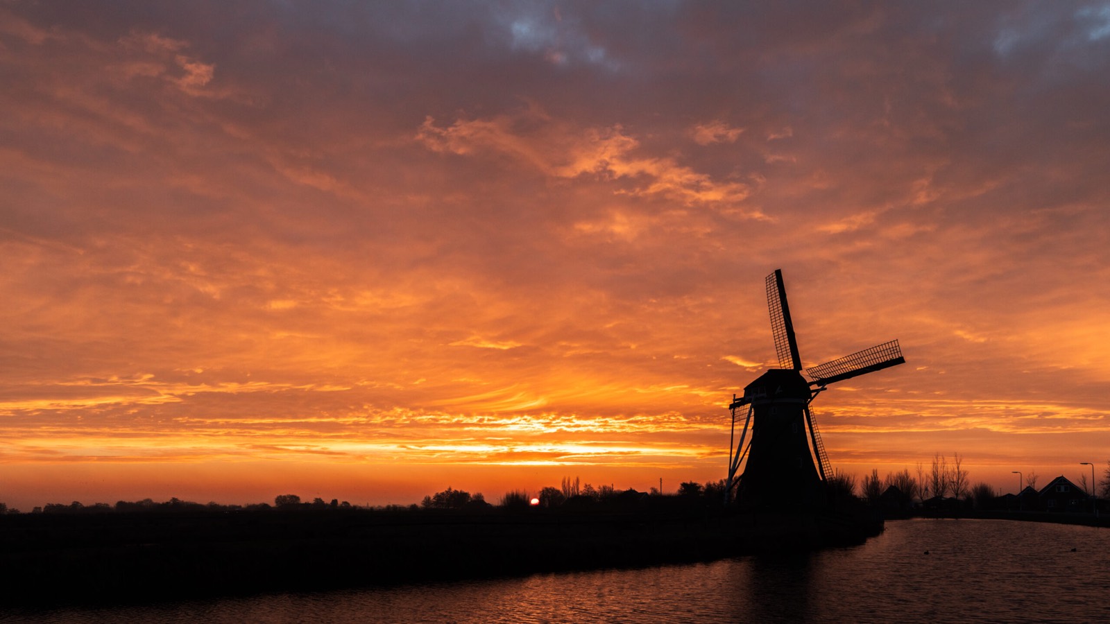 Molen als silhouet tegen een oranje zonsondergang